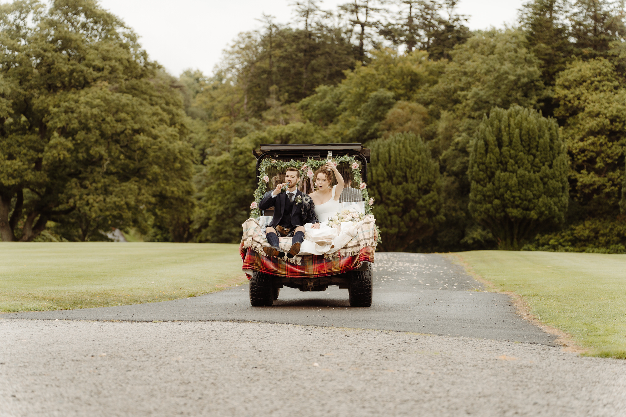 Bride and groom cheer with champagne on a golf buggy at Kinmount House wedding