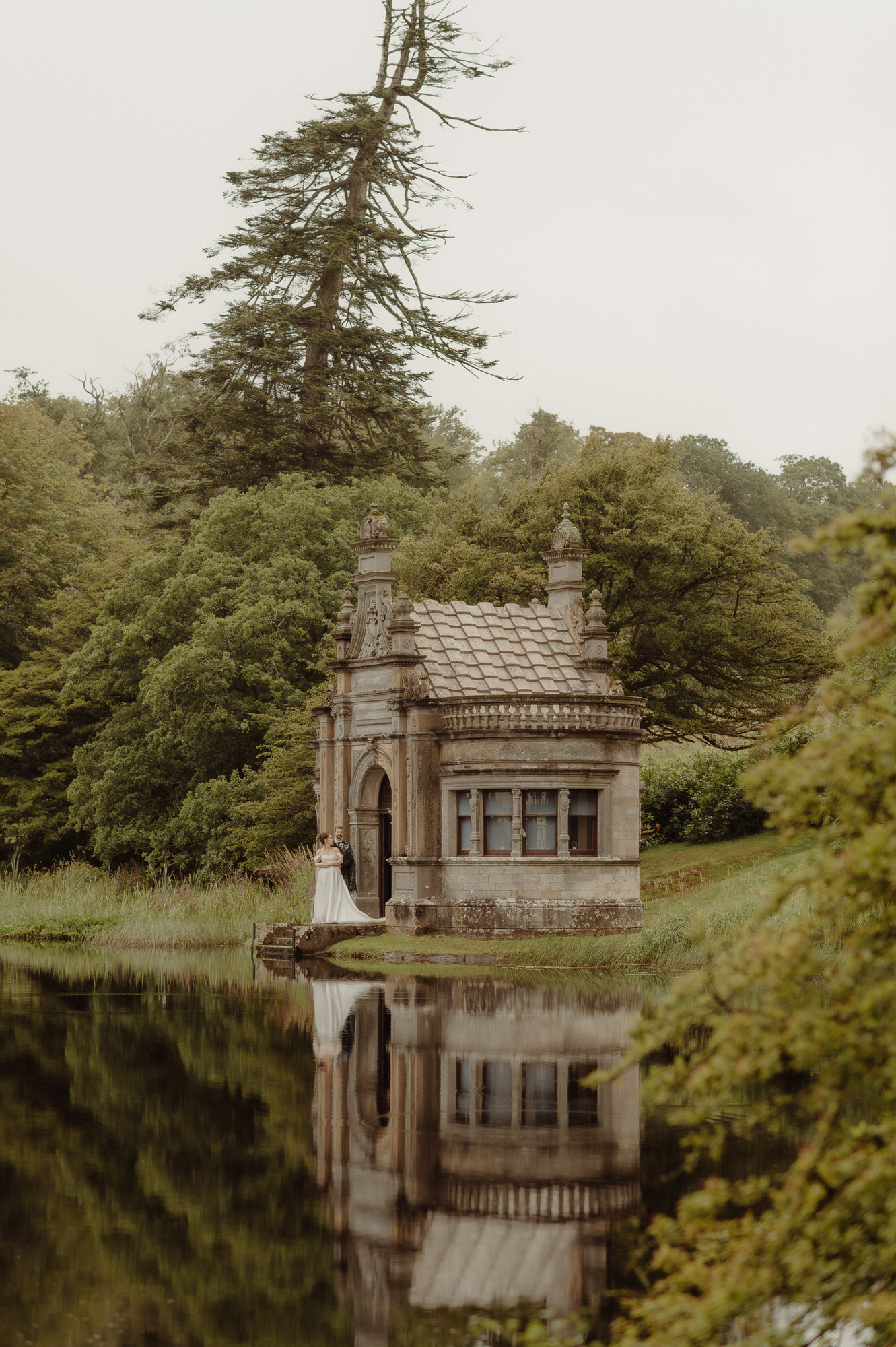 Couple stand near the lake in the boating house at Kinmount House wedding