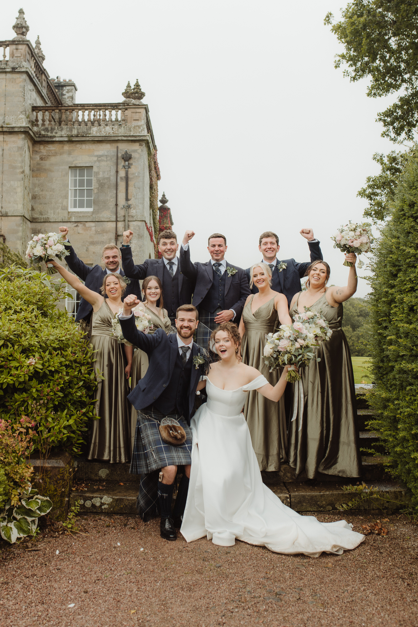 Blue and olive green bridal party cheer on stone steps at Kinmount House wedding