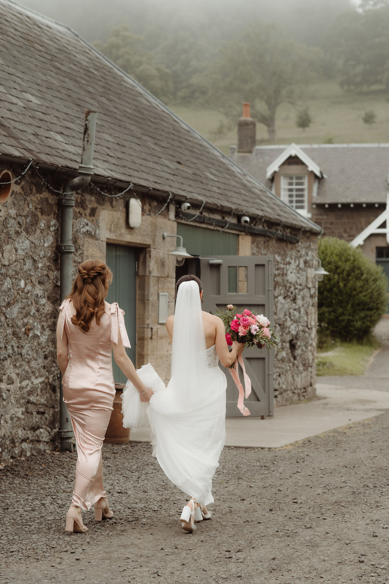 Bride walks towards a green door helped by her bridesmaid at the Byre at Inchyra.