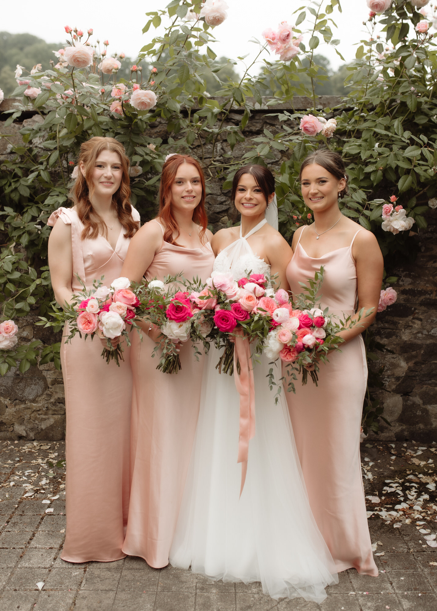 Colourful pink bridesmaids stand beside a bride surrounded by pink roses at the Byre at Inchyra.