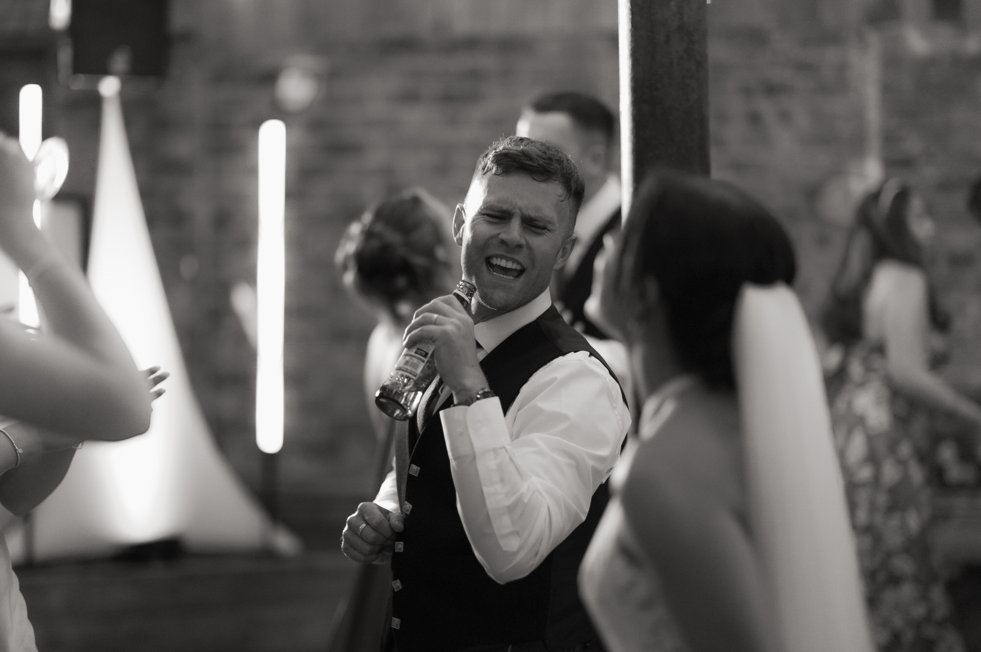 Groom holds a bottle and pretends it's a microphone in black and white at the Byre at Inchyra.