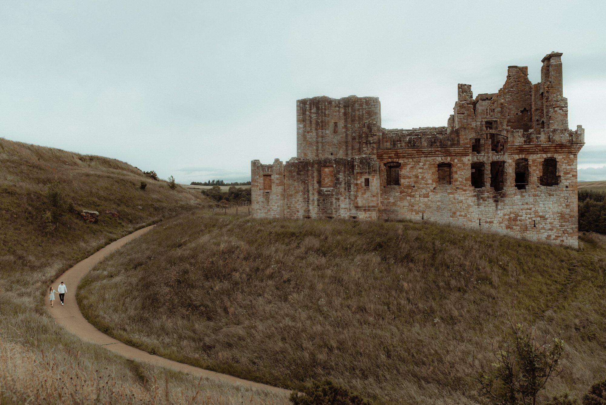 Couple walk beneath Crichton Castle ruins in Scotland.