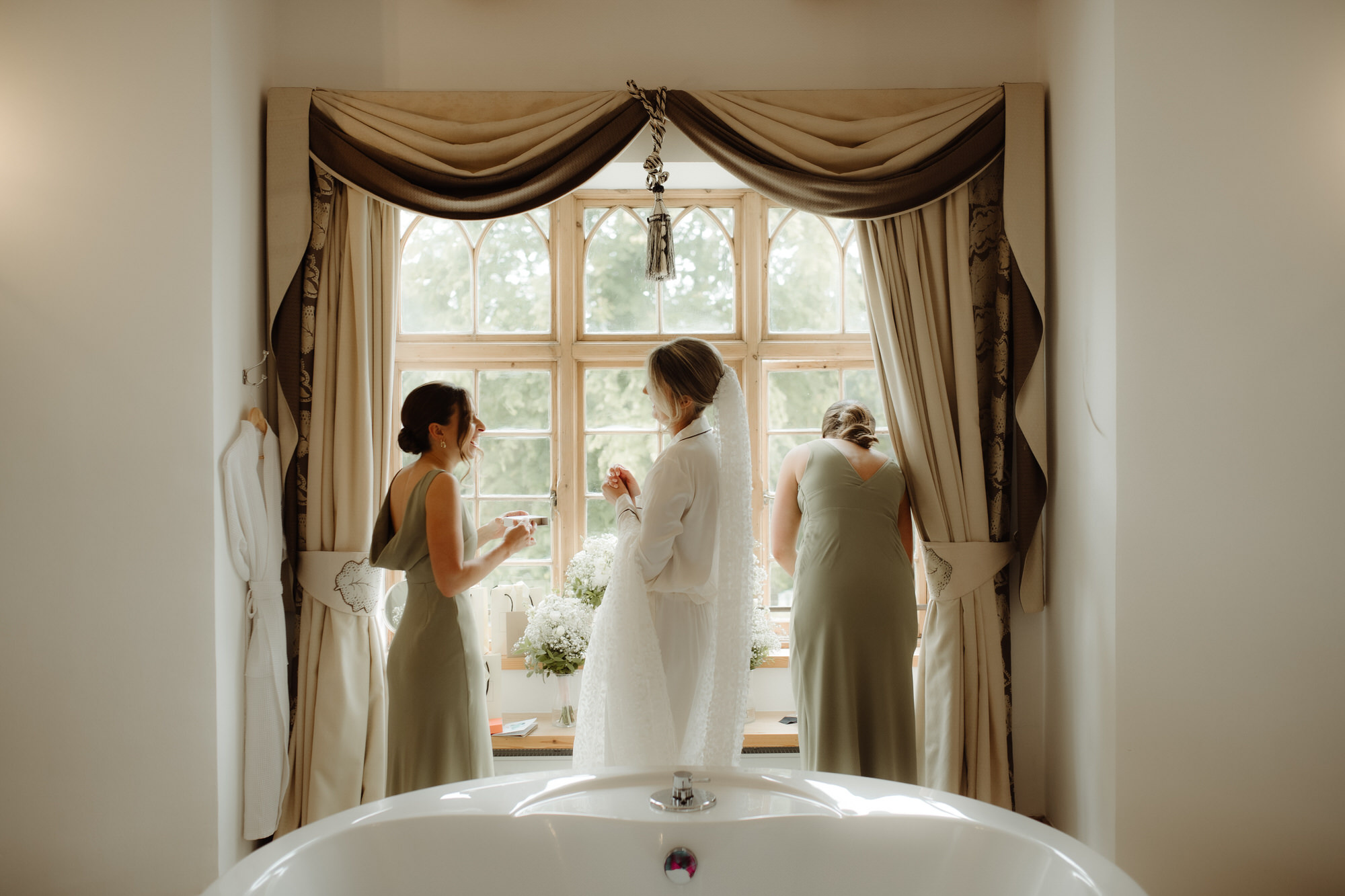 Bride stands with two bridesmaids in a window of Achnagairn Castle. 