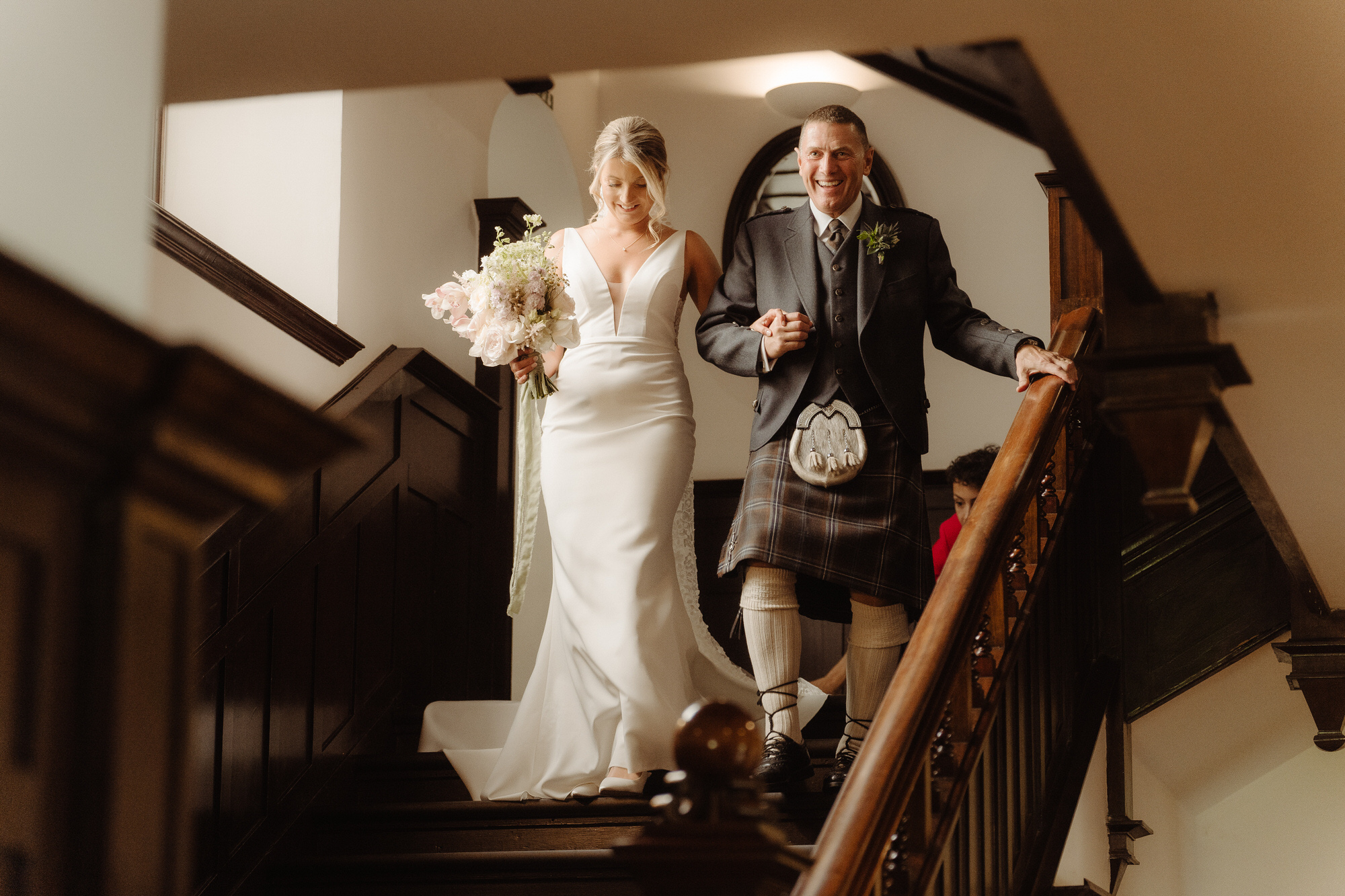 Bride and her smiling father decend stairs at Achnagairn Castle.