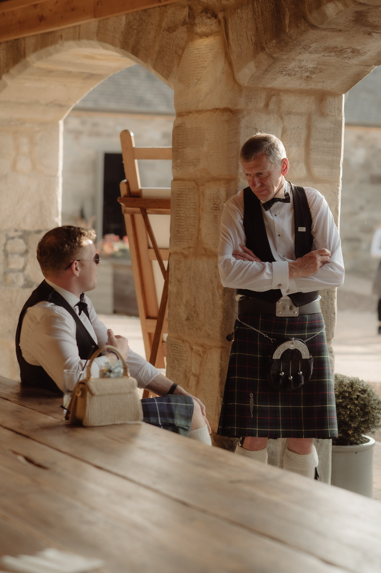 Two men talk in the sunshine at Edinburgh wedding.