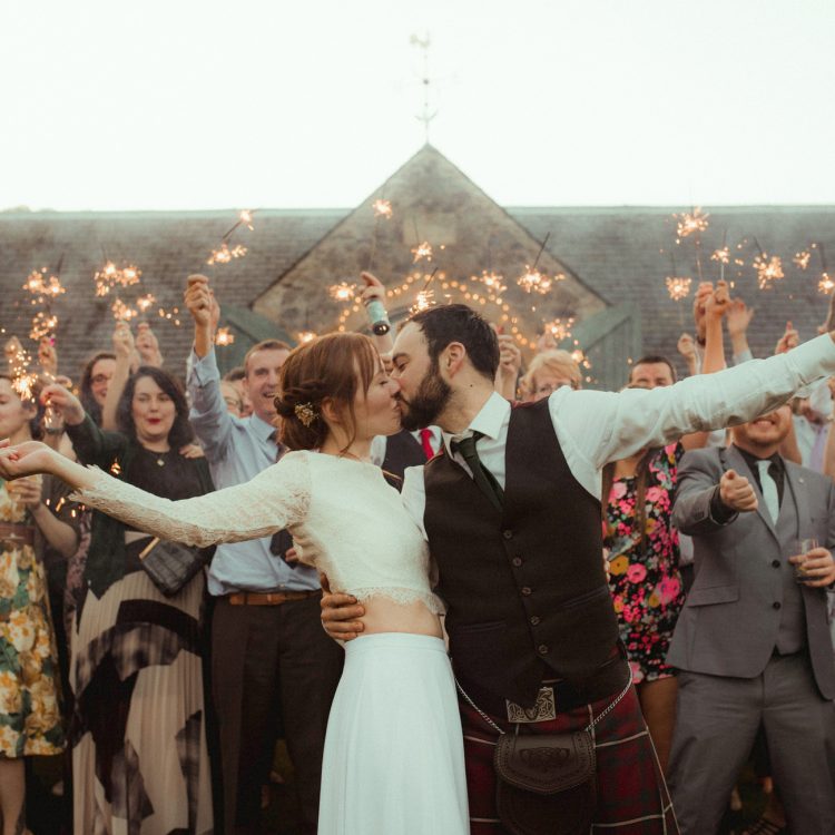 Couple kiss under sparklers with The Byre at Inchyra in the background.